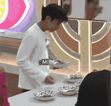 a man in a white shirt is standing in front of a table with bowls of food and a sign that says mi