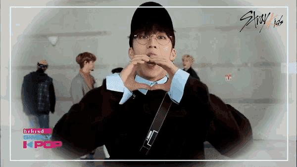 a man wearing glasses and a hat is making a heart shape with his hands behind the words behind simply kpop