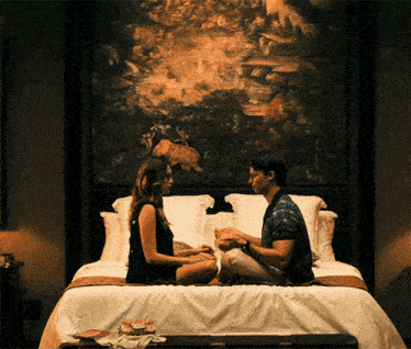 a man and woman are sitting on a bed in front of a painting