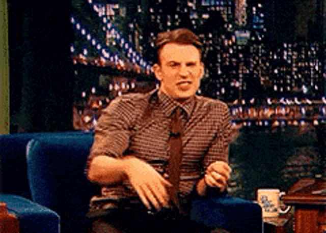 a man in a plaid shirt and tie sitting in a chair