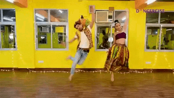 a man and a woman are jumping in the air in front of a yellow wall in a dance studio .