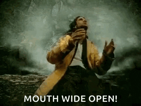 a man in a suit and tie is holding a microphone in his mouth and says mouth wide open .