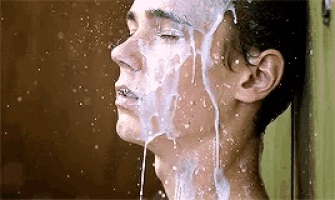 a young man is taking a shower with a lot of foam on his face .