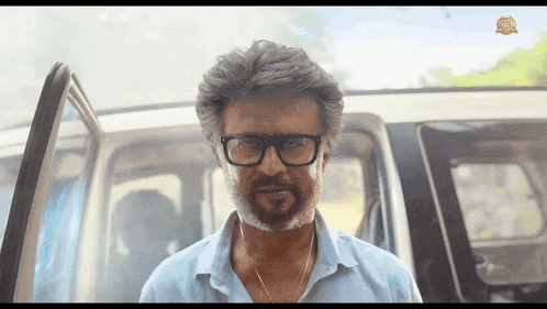 a man with glasses and a beard is standing in front of a car with the door open
