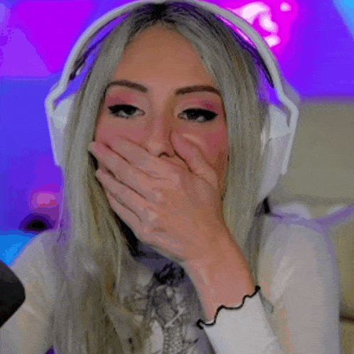 a woman wearing headphones is covering her mouth with her hand while sitting in front of a microphone .