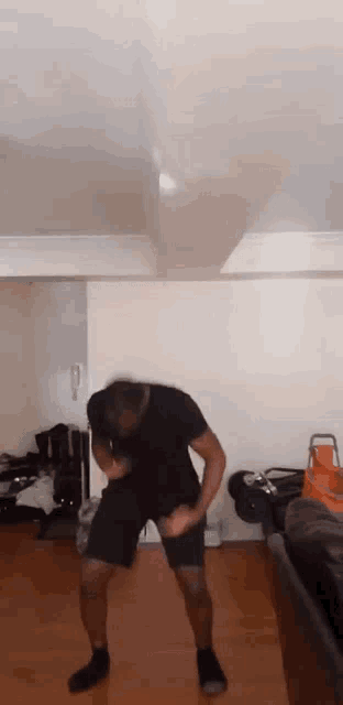 a man is dancing in a living room while wearing shorts and a black shirt .
