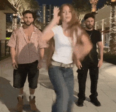 two men and a woman are dancing on a sidewalk at night