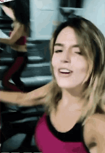 a woman in a pink tank top is smiling while riding a treadmill