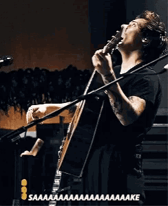 harry styles is singing into a microphone while playing a guitar .