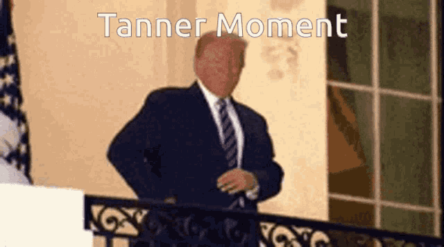 a man in a suit and tie stands on a balcony with the words tanner moment written above him