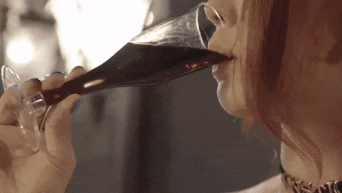 a woman drinking a glass of wine with a necklace on her neck