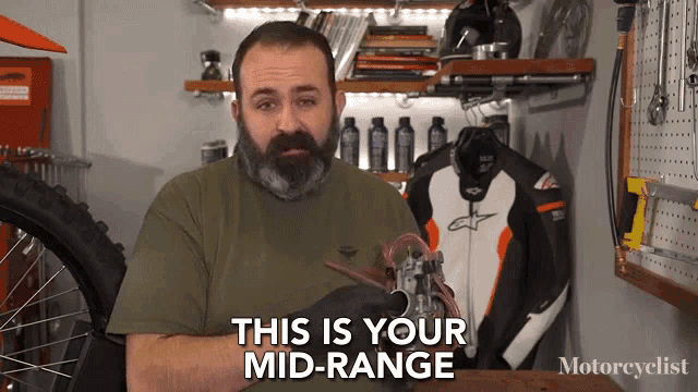a man with a beard says this is your mid-range in front of a motorcycle