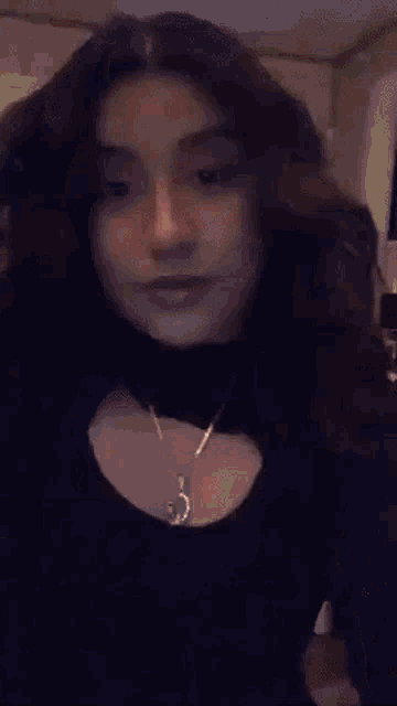 a young girl wearing a black dress and a necklace is taking a selfie .