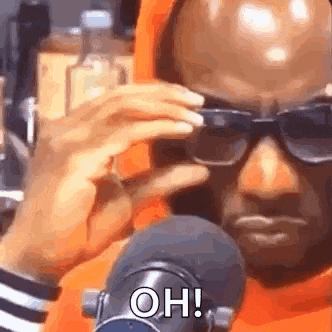 a man wearing sunglasses is sitting in front of a microphone and talking into it .