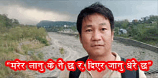a man with a backpack is standing in front of a river with mountains in the background .
