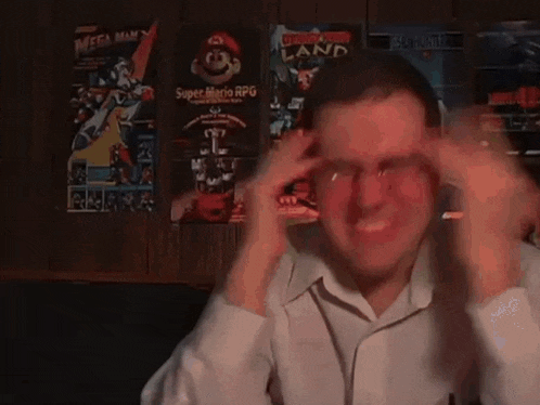 a man is holding his head in front of a wall with posters for super mario rpg and mega man