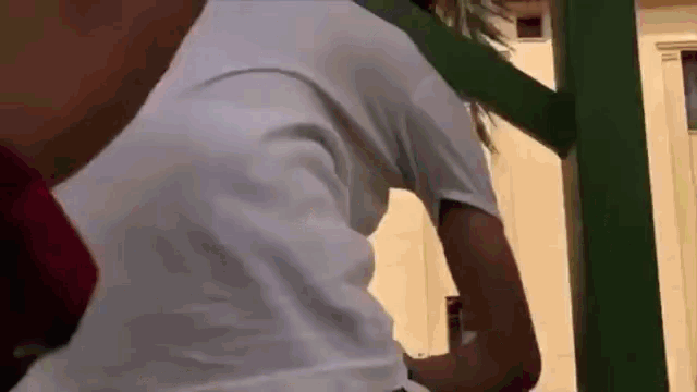 a person wearing a white t-shirt is standing next to a green pole .