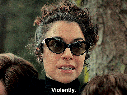 a woman wearing sunglasses and a black turtleneck is saying violently