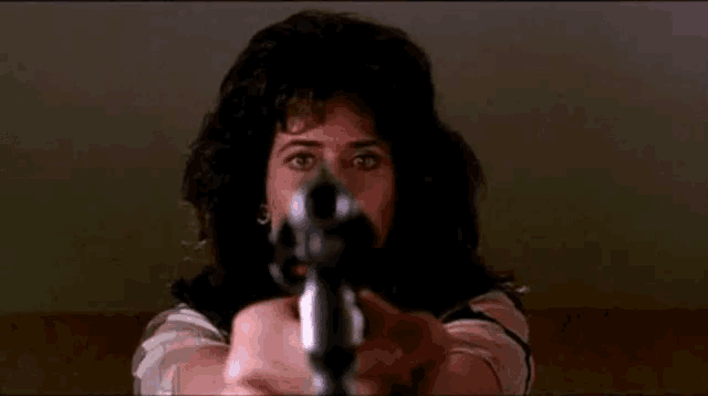 a woman with curly hair is pointing a gun at the camera