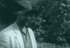 a man in a suit and hat is standing in front of a red umbrella .