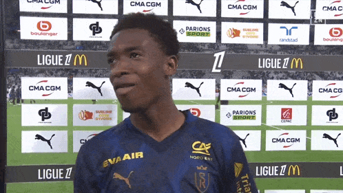 a soccer player stands in front of a wall that says ligue z mcdonald 's and cma cgm