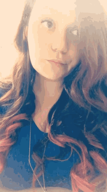 a woman with red hair is wearing a blue shirt and a necklace