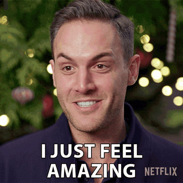 a man is smiling and says " i just feel amazing " in front of a christmas tree