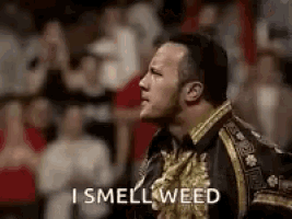 the rock is standing in front of a crowd and smelling weed .