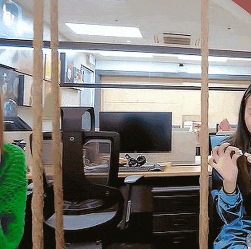 a woman sits in a cubicle behind a rope fence with a computer monitor in the background