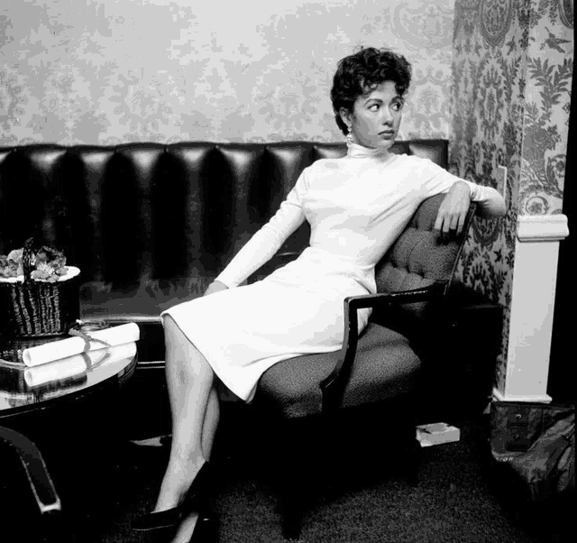 a woman in a white dress sits in a chair in front of a couch
