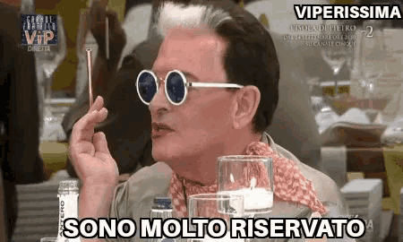 a man wearing sunglasses and a scarf is smoking a cigarette while sitting at a table .