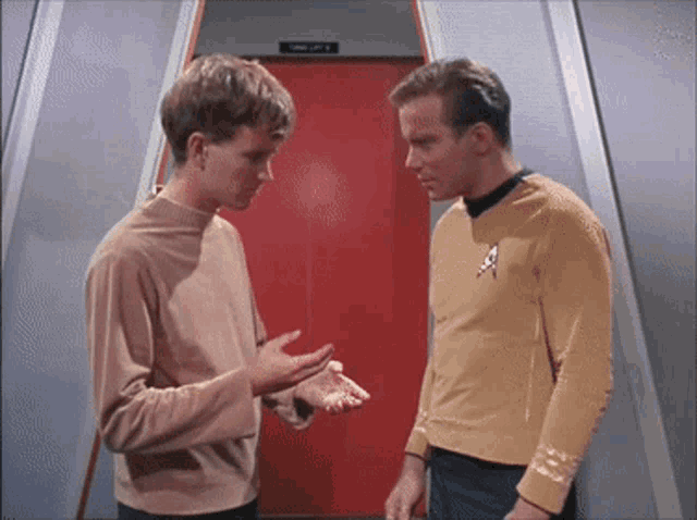 two men are talking in front of a red door that says " crew lift "