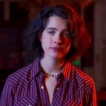a woman wearing a purple striped shirt and a necklace is smiling in a dark room .