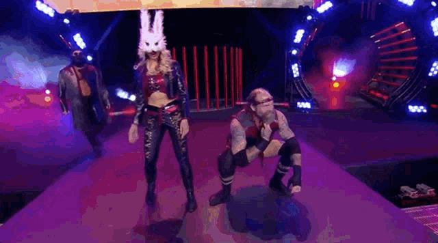 a woman in a bunny mask is standing next to a man in a kneeling pose on a stage .