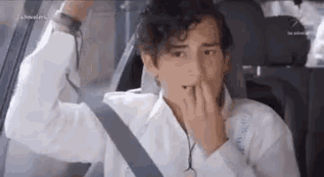 a young man is sitting in the back seat of a car with his hands on his face .