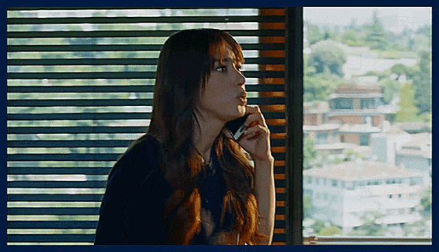 a woman talking on a cell phone in front of a window with blinds