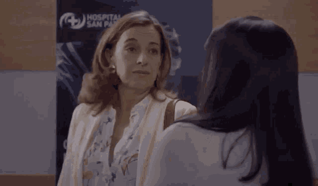 two women are standing next to each other and looking at each other in front of a hospital sign .