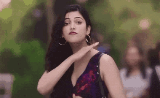 a woman in a purple dress and hoop earrings is standing in front of a group of people .