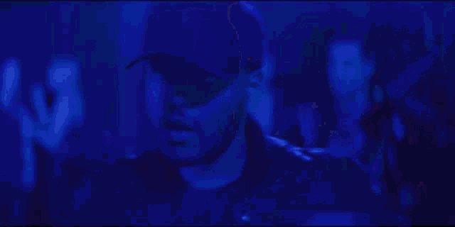 a man wearing a hat is standing in a dark room with blue lights behind him .