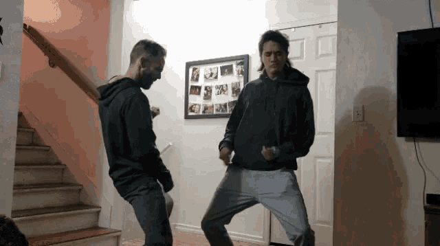 two men are dancing in a living room with a picture on the wall that says " i love you "