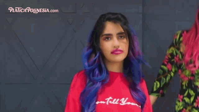 a woman with purple hair is wearing a red shirt that says " you tell yours "