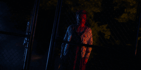 a man with blood on his face is behind a chain link fence holding a torch