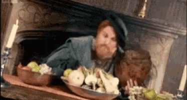 a man is sitting in a fireplace with a bowl of fruit on the table .