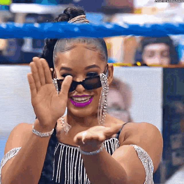 a woman wearing sunglasses and earrings is smiling and waving at the camera .