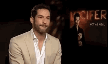 a man in a suit is sitting in front of a sign that says `` hot as hell '' .