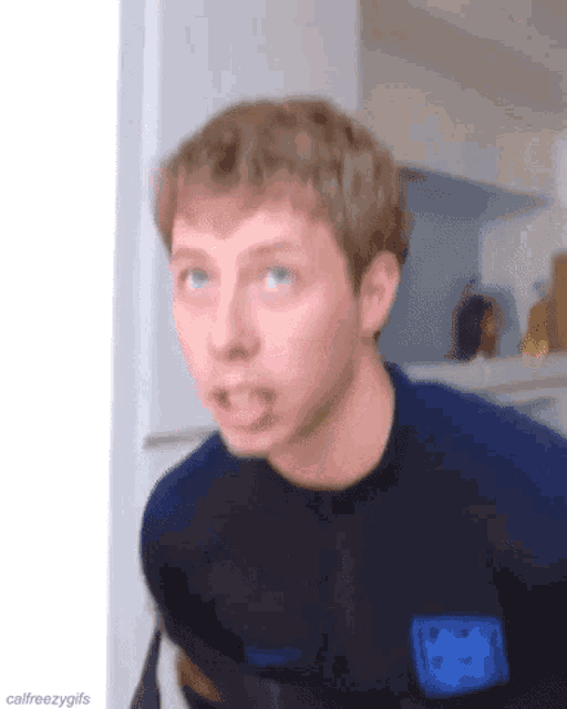 a young man in a blue shirt is making a funny face while standing in a kitchen .