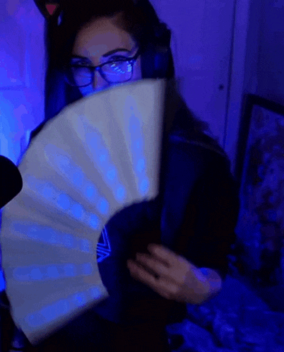 a woman wearing glasses is holding a white fan in front of her face .