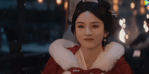a woman in a red dress with a white fur collar is smiling .