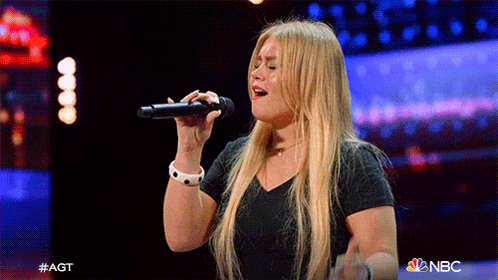 a woman singing into a microphone with nbc behind her