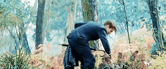 a man in a suit is kneeling down in the woods with a sword .